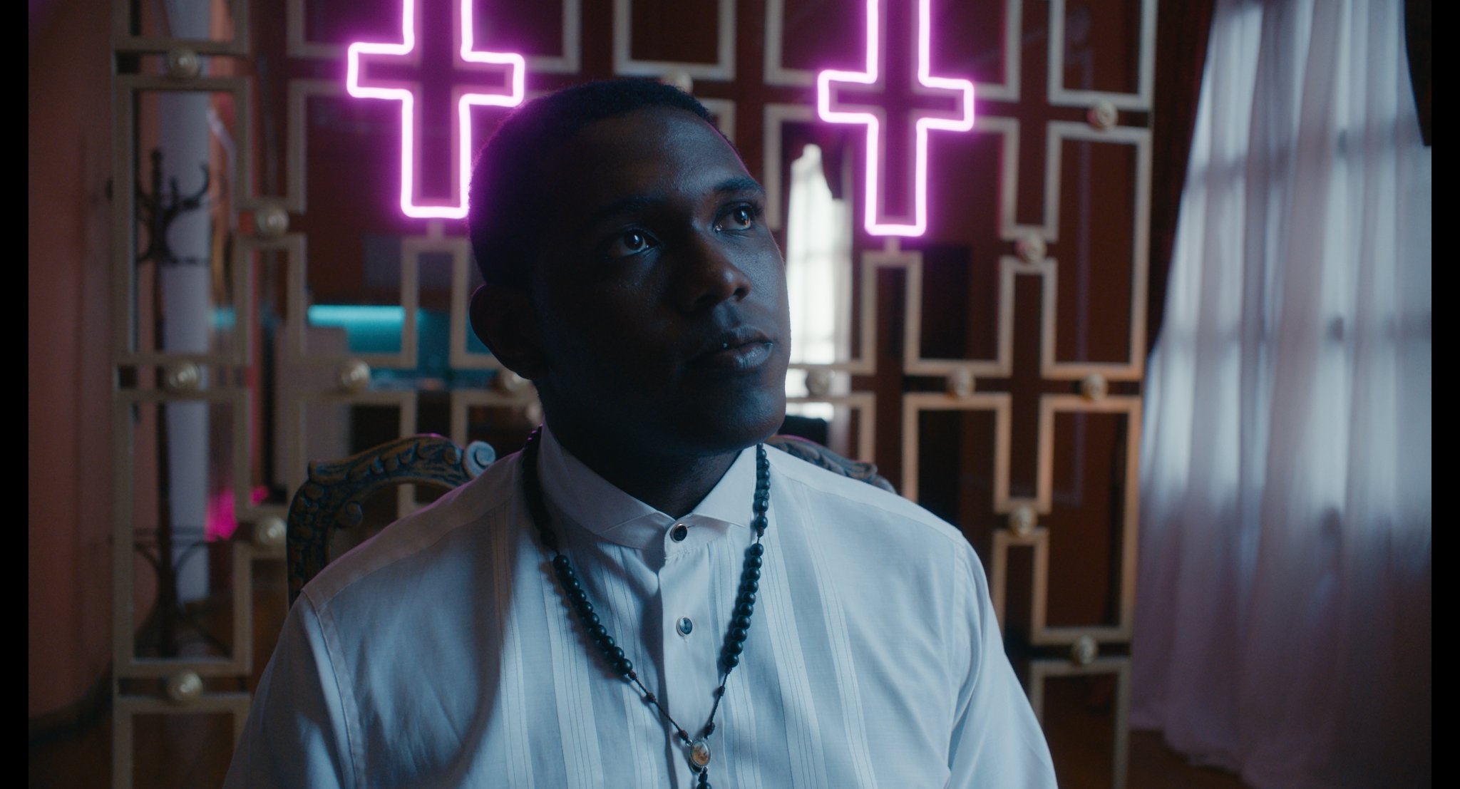 A character in white beneath pink neon crosses